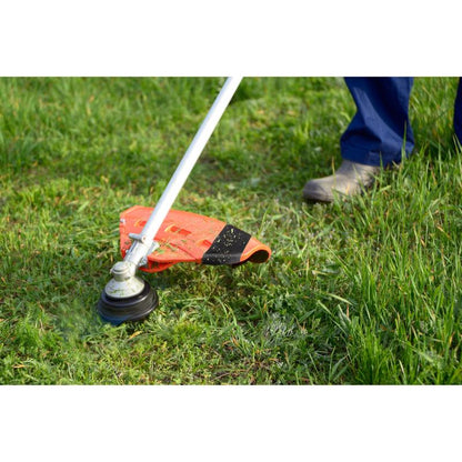 With sturdy boots, a person trims the green grass in the garden, while a roll of Scotch® Extremium™ Ultra High Performance Tape DT17 (10 m x 24 mm) by 3M lies nearby, ready for demanding repairs.