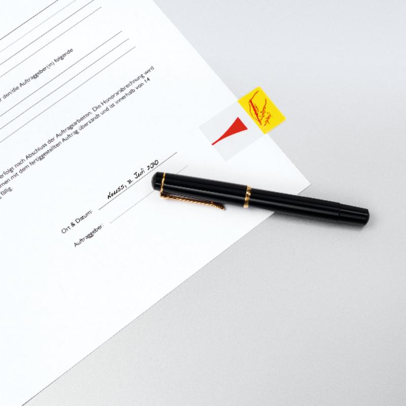 A black fountain pen lies on a white surface next to a partially visible document with a signature line and a yellow 3M Post-it® Index Tab, Standard (25.4 x 43.2 mm, 50/dispenser), marking the corner.