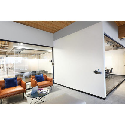 A modern office waiting area with two brown leather armchairs, blue cushions, a glass coffee table with a laptop and notebook, and glass meeting rooms equipped with the Post-it® Easy Erase Whiteboard Surface from 3M Deutschland GmbH.