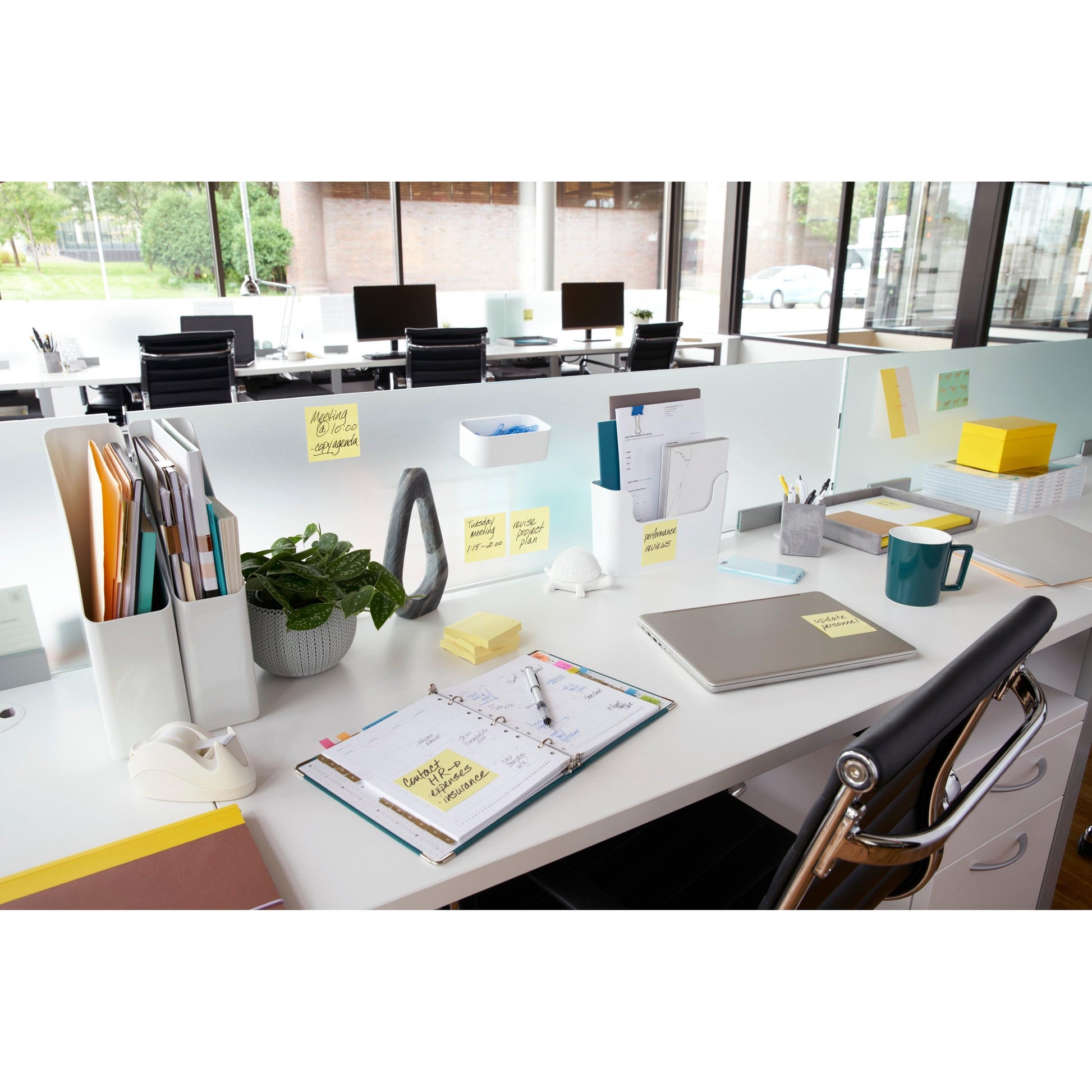 Ein moderner Bürotisch mit Laptop, Planer, Tasse, Topfpflanze, Schreibwaren und Post-it® Notes (76x76 mm, Gelb) der 3M Deutschland GmbH - Aktionspackung mit 16+4 Blöcken im PEFC-zertifizierten Karton - ist in der Nähe heller Bürofenster organisiert.