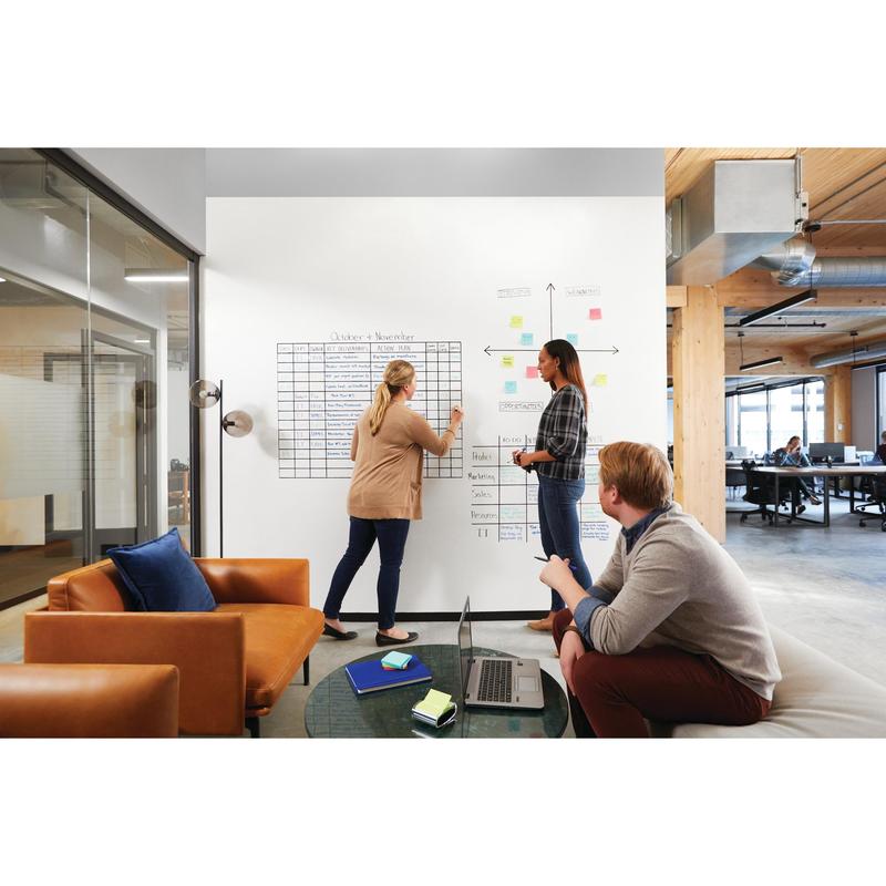 Three people sit in a modern office. Two are using the Post-it® Easy Erase Whiteboard Surface, white from 3M Deutschland GmbH, adding charts and sticky notes; one sits on a couch with a laptop. Large windows and an open work area are visible.