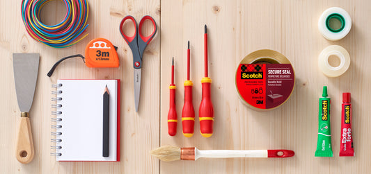 Verschiedene Werkzeuge und Verbrauchsmaterialien, darunter der 3M Deutschland GmbH Abroller mit Pistolengriff + Scotch® Verpackungsklebeband (50 mm x 66 m, Braun, 1 Spender + 2 Rollen/Packung), ausgestellt auf einer Holzfläche.