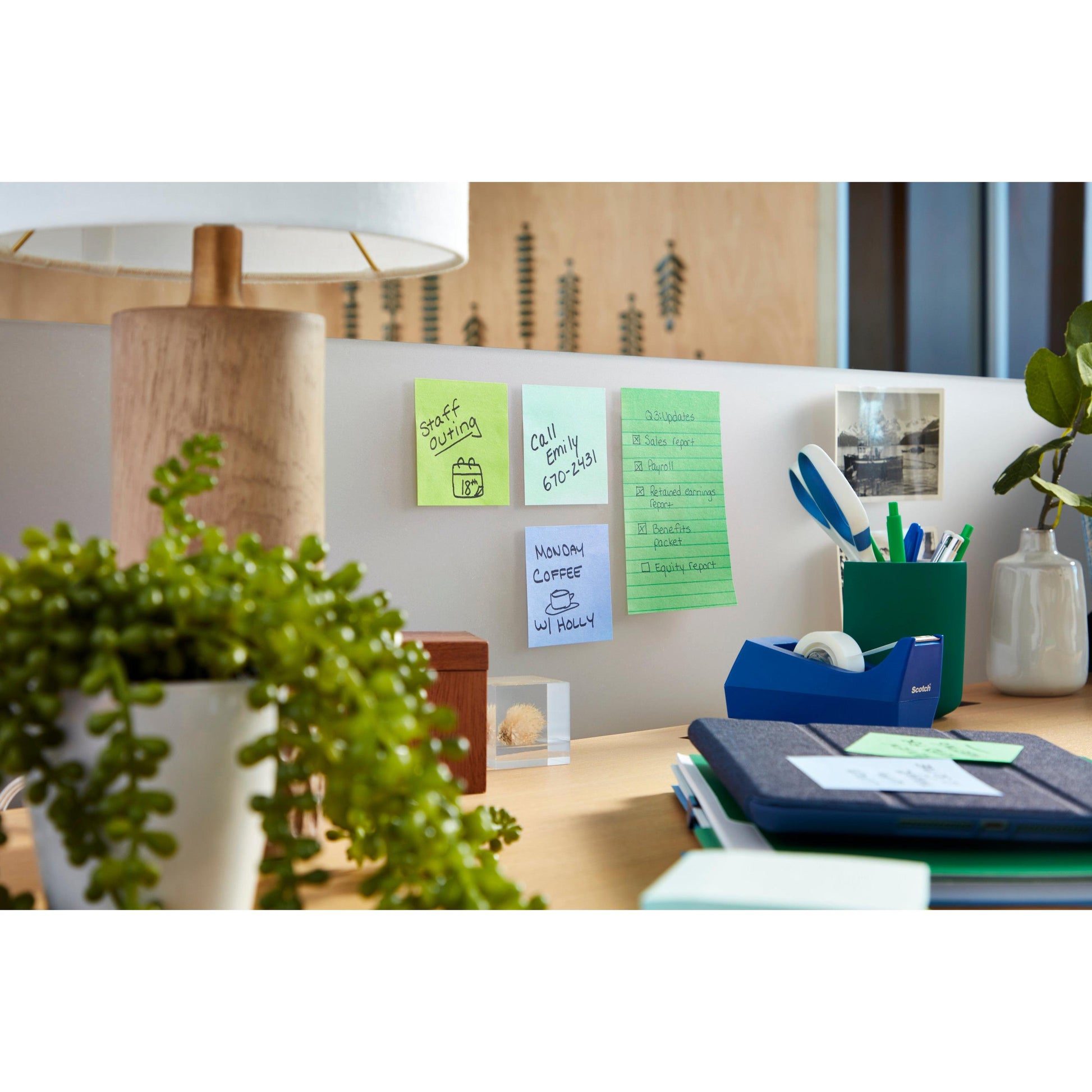 Ein Schreibtisch mit Lampe, Pflanze und 3M Deutschland GmbH Post-it® Super Sticky Notes (76 mm x 127 mm, 90 Blatt/Block, 100% PEFC), Büromaterial, Mappen, Klebebandabroller, Stifte, ein Foto und natürliches Licht.