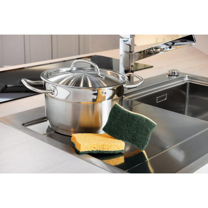 A stainless steel pot with a lid stands on a kitchen countertop next to a sink. In front of the pot are two Scotch-Brite® Classic Cleaning Sponges from 3M Deutschland GmbH, lying on the countertop.