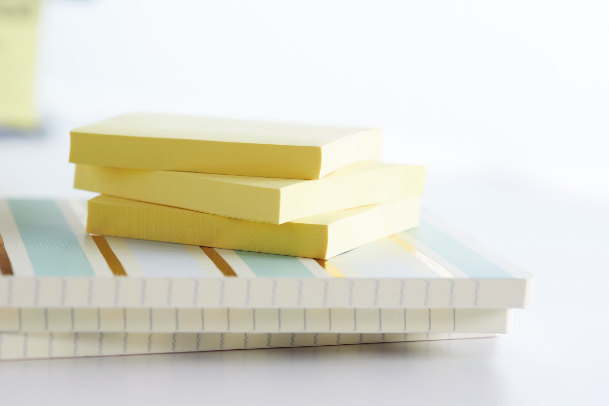 Drei Stapel Post-it® Recycling Notes (38 mm x 51 mm, 100 Blatt, 100% PEFC) der 3M Deutschland GmbH liegen auf zwei geschlossenen, gestreiften und linierten Notizbüchern vor einem sanft verschwommenen Hintergrund.