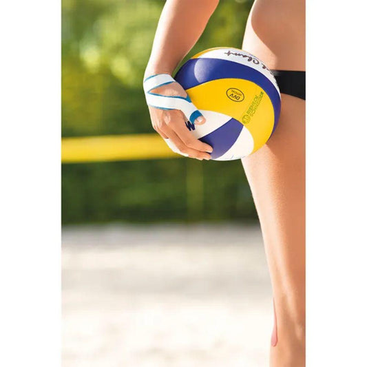 Eine Person in schwarzer Badebekleidung steht auf einem Sandplatz und hält einen blau-gelb-weißen Volleyball in der Hand. Ihre rechte Hand ist mit Leukotape Sport Tape Classic weiß 3,75 cm x 10 m der BSN Medical GmbH umwickelt. Im Hintergrund sind ein unscharfes Netz und Bäume zu sehen.