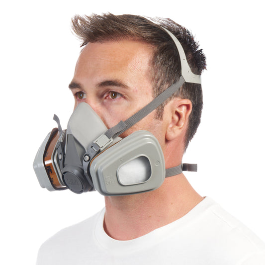 Ein Mann mit kurzen braunen Haaren trägt ein weißes Hemd und die 3M™ Atemschutzmaske 6002KIT-1 (A2P2) der 3M Deutschland GmbH mit verstellbaren Gurten und Doppelpatronen, die von den Schultern aufwärts vor einem schlichten weißen Hintergrund gezeigt wird.
