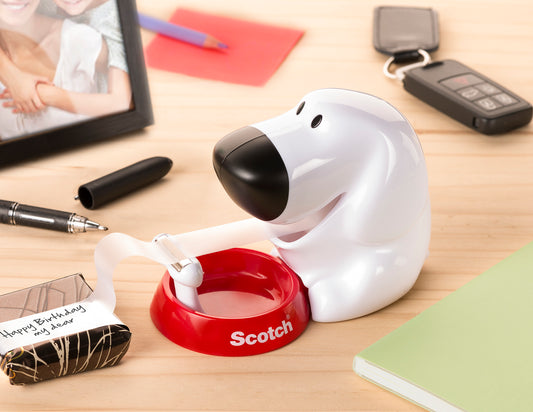 Der Scotch™ Tischabroller im Hunde Design C31 mit Scotch® Magic™ Klebeband (19 mm x 8,89 m) von 3M Deutschland GmbH steht auf einem Holzschreibtisch neben Notizbuch, Stift, Schlüsselanhänger, Geschenk und gerahmtem Foto.