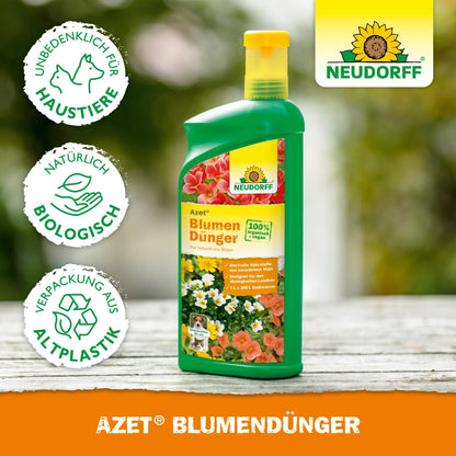 A green bottle of Neudorff Shop Azet Liquid Flower Fertilizer stands on wood. The label features flowers and symbols indicating that this liquid fertilizer is pet-safe, natural, and in a bioplastic packaging for healthy plant growth.