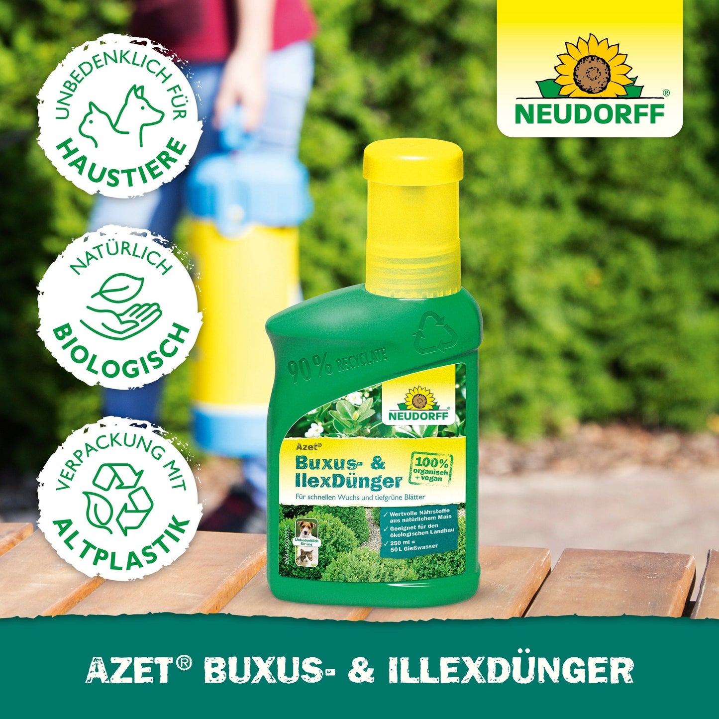 A green bottle of Neudorff Shop Azet Buxus- & IlexFertilizer liquid stands on a wooden surface outdoors. Icons show pet safety, biological ingredients, and recycled packaging. The Neudorff logo appears in the upper right corner.