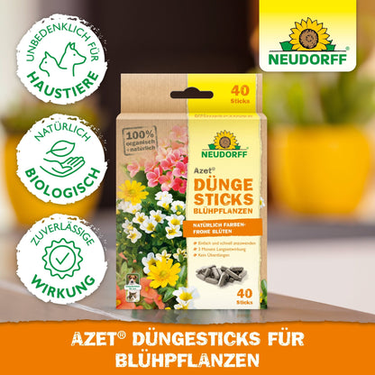 A box of Azet Fertilizer Sticks for flowering plants from Neudorff Shop (40 sticks) is shown in front of blooming flowers. The packaging emphasizes safety for pets, natural ingredients, and reliable effectiveness.