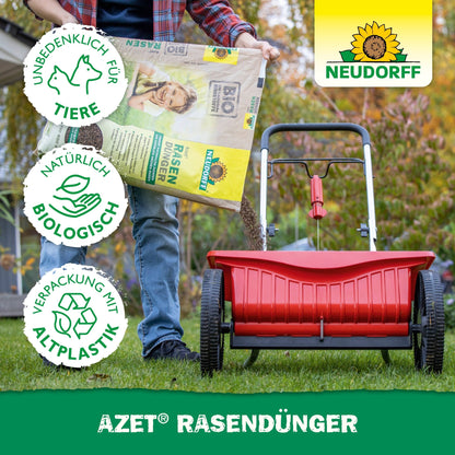 A person fills a red spreader with Neudorff Shop Azet Lawn Fertilizer 2.5-5 kg to promote dense lawn areas. Three symbols indicate it is pet-friendly, biologically natural, and made from recycled plastic. The Neudorff logo is visible.