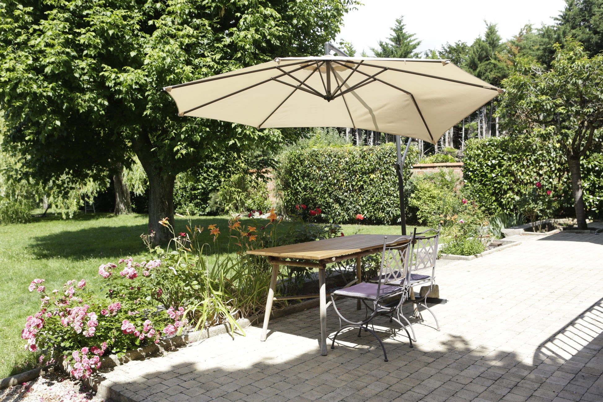 Ein Holztisch mit zwei Metallstühlen steht auf einer Terrasse unter einem beigen Sonnenschirm, der im Garten mit 3M Scotch® Extremium™ Ultra Hochleistungs-Klebeband DT17 (25 m x 48 mm) befestigt wurde.