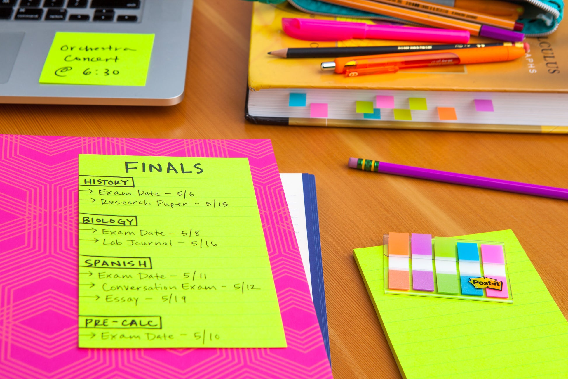 Auf einem Studientisch liegen Bücher, Stifte, eine pinke Mappe mit dem Terminplan für die Abschlussprüfungen auf Neonpapier und Post-it® Super Sticky Notes im Großformat (101 mm x 101 mm, 70 Blatt/Block, 100% PEFC) von 3M Deutschland GmbH, alles fein säuberlich auf Holz angeordnet.