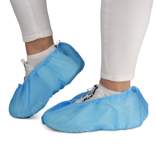 A person is wearing white pants and sneakers with ARNOMED ABS shoe covers from ARNOWA GmbH. These non-slip, disposable shoe covers (pack of 100) protect shoes and floors—ideal for hygienic environments.