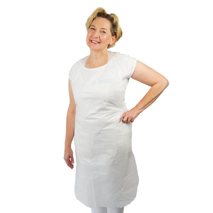 Eine Person steht lächelnd mit einer Hand an der Hüfte und trägt die ARNOMED COVER PE-SCHÜRZE Geblockte Einmalschürzen aus PE von ARNOWA GmbH über einem weißen Hemd und einer Hose vor einem schlichten weißen Hintergrund.