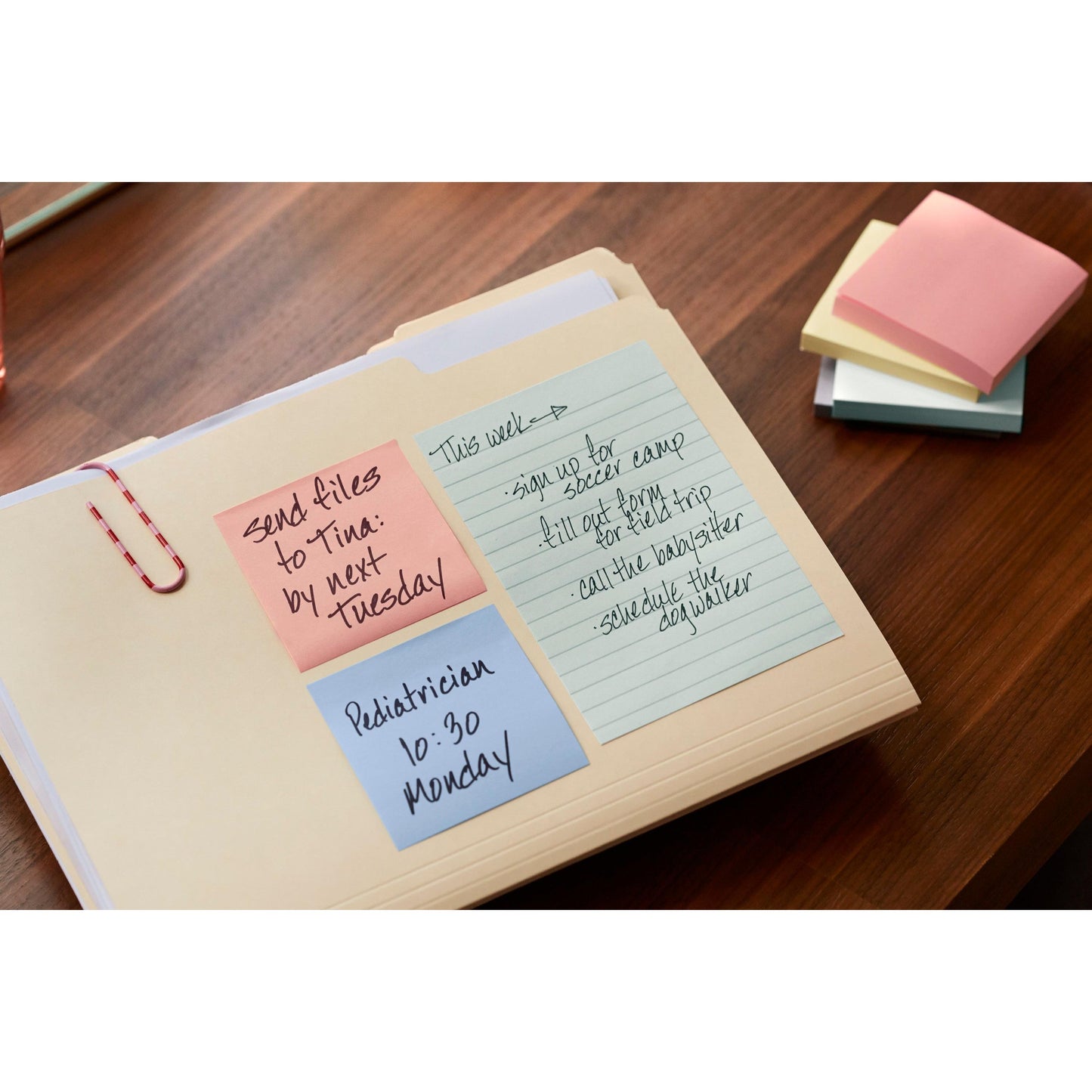 A binder on the wooden desk with 3M Deutschland GmbH Post-it® Recycling Notes (76 mm x 76 mm, 100 sheets/block, 100% PEFC) lists tasks such as sending files to Tina, a pediatrician appointment, and other to-dos; additional sticky notes lie next to it.