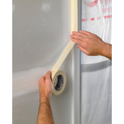 Eine Person klebt Scotch® Abdeckband Basic, 50 m von 3M Deutschland GmbH entlang der Kante eines kunststoffverkleideten Fensterrahmens, wahrscheinlich als Vorbereitung für Maler- oder Bauarbeiten.