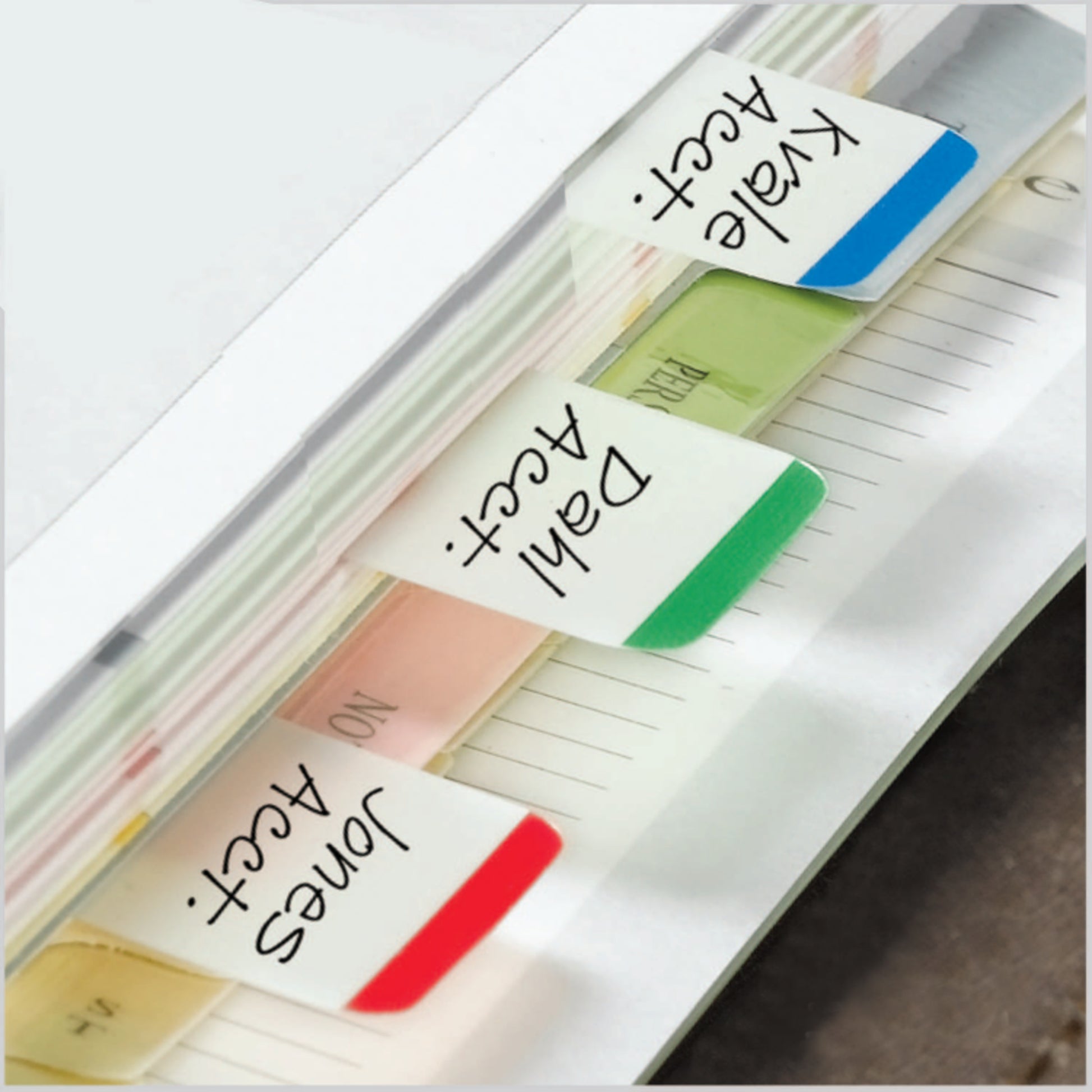 Eine Nahaufnahme zeigt 3M Post-it® Index Strong Ablagetabs in verschiedenen Farben (25,4 mm x 38,1 mm) mit den Bezeichnungen "Jones Acct", "Dahl Acct" und "Kvale Acct" nebeneinander in einem Ordner. Jede Packung enthält 66 Registerkarten.