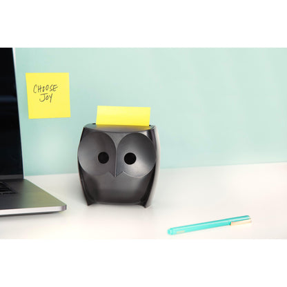 A black Post-it® Z-Notes Dispenser "Owl" (3M Deutschland GmbH) with yellow Super Sticky Z-Notes stands on a white desk, next to a laptop and a blue pen. A "CHOOSE JOY" note hangs on the wall against a light blue background.