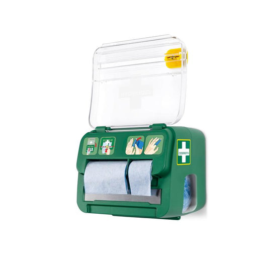 Der grüne, an der Wand montierte Cederroth Weichschaumbinde 2-in-1 Spender von Orkla Wound Care AB fasst sechs Verbände, hat einen transparenten Deckel mit Kreuzsymbol, blaue Papierrollen, eine bebilderte Anleitung und ein gelbes Werkzeug für die Notfall-Wundversorgung auf der Oberseite.