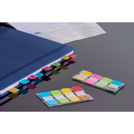 Ein blaues Notizbuch mit beschrifteten farbigen Trennblättern liegt auf einem Schreibtisch neben Papierblättern. Daneben liegen zwei Packungen Post-it® Index Strong Ablagestifte der 3M Deutschland GmbH in den Farben gelb, rot, blau und grün (15,8 x 38,1 mm, 40 Stifte/Packung).