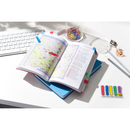 An open card book with colored tabs lies on a blue notebook on a white desk next to office supplies and 3M Post-it® Index Arrows (11.9 mm x 43.2 mm, 100 sticky notes/dispenser) - perfect for organizing documents and marking pages.