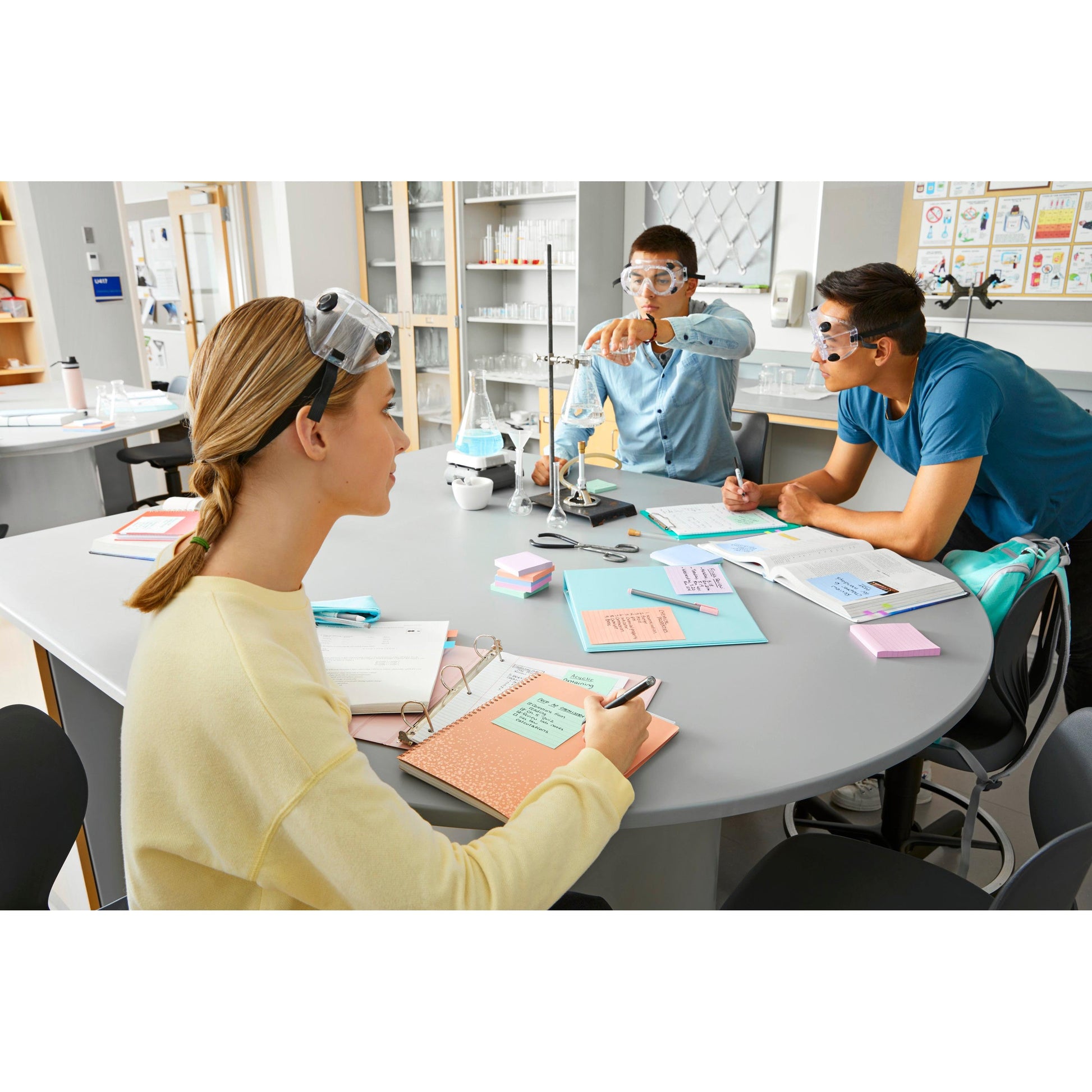 Drei Studenten mit Schutzbrillen arbeiten an einem Labortisch zusammen. Während einer die Geräte einstellt, machen die anderen Notizen mit Post-it® Super Sticky Notes (47,6 mm x 47,6 mm, 90 Blatt/Block, 100% PEFC) der 3M Deutschland GmbH.