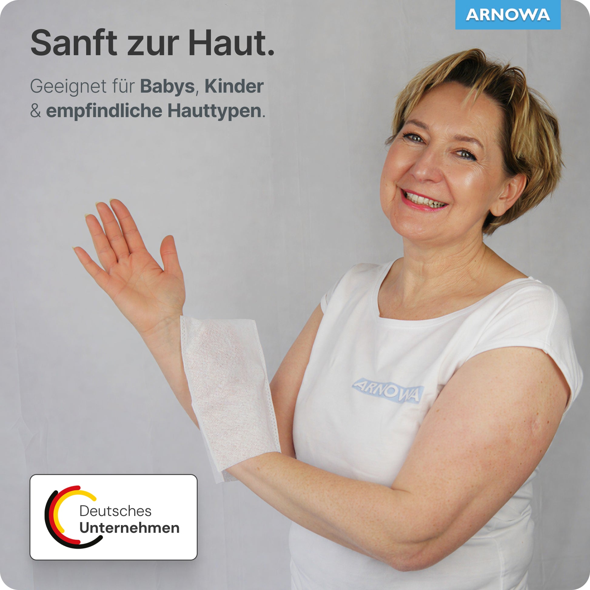 Eine Frau in einem weißen Hemd lächelt, während sie einen ARNOMED Einmalwaschhandschuh Spunlace mit PE, wasserabweisend (Beutel, 50 Stück) der ARNOWA GmbH über den Arm hält. Der deutsche Text hebt die sanfte Pflege für Babys, Kinder und empfindliche Haut hervor.