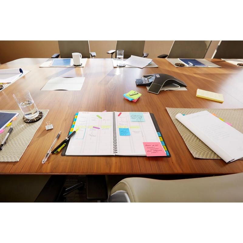 A conference room table with an open planner, the Post-it® Z-Notes Dispenser Cat White from 3M Deutschland GmbH, Post-it® Super Sticky Z-Notes Pink (76x76 mm, 90 sheets), pens, notepads, water glasses, and office supplies. Several chairs surround the table.