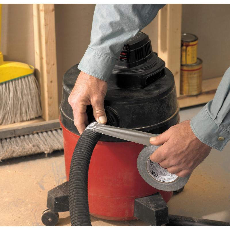 Someone wraps Scotch® Extremium™ Universal Adhesive Tape (3 m x 19 mm) from 3M Deutschland GmbH around the hose of a red-black workshop vacuum. A broom and paint cans lie on the dusty floor of a construction site.