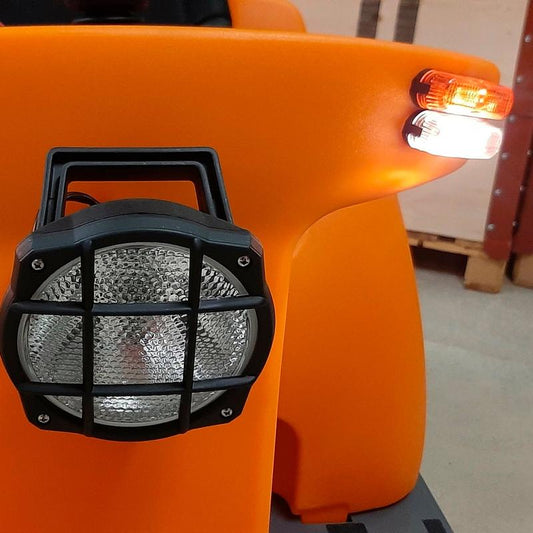 Nahaufnahme eines Balimat Straßensets der Diversey Deutschland GmbH & Co. OHG, mit rundem Scheinwerfer mit schwarzem Gitter und Seitenleuchten, bereit für den Straßenverkehr in einem Lager mit Paletten; geeignet für die Aufrüstung des Balimat 6500/6500HD.