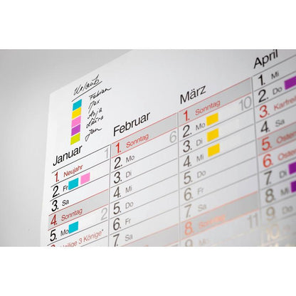 Close-up of a wall calendar for January to March with colorful 3M Deutschland GmbH Post-it® Index Tabs (Mini, 11.9 x 43.2 mm) as color-coded markers for each person's handwritten appointments or activities.
