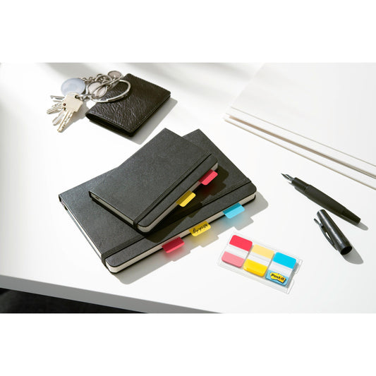 Ein schwarzes Notizbuch, ein Portemonnaie mit Schlüsseln, ein Stift, ein Marker und 3M Post-it® Index Strong Ablagetabs (Rosa & Grün) liegen fein säuberlich auf einem weißen Schreibtisch neben Papieren.