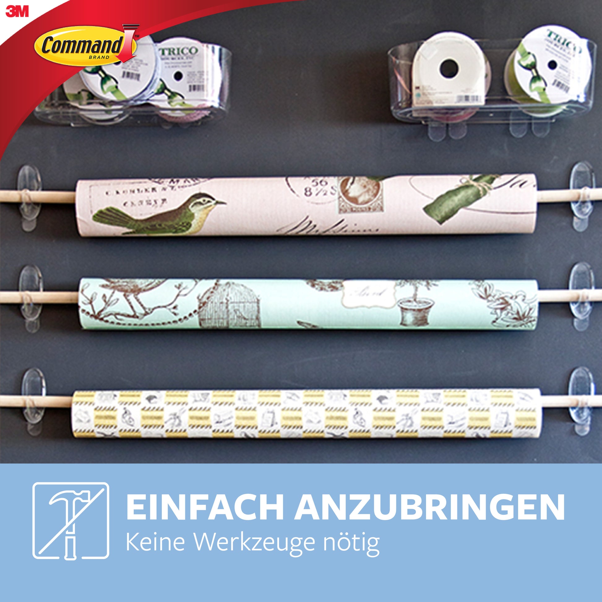 Drei Rollen Dekorationspapier hängen an weißen Stangen, die mit 3M Command™ Haken M, transparent (17091CLR), an der Wand befestigt sind. In der Nähe befinden sich Klebebandrollen und Abroller. Deutscher Text: "Einfach Anbringen. Keine Werkzeuge nötig.