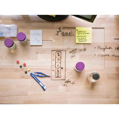 On a wooden table are bottles, a water bottle, a utility knife, small parts, a notebook, and handwritten notes with diagrams. In the upper right corner is a 3M Post-it® Super Sticky Note (101 mm x 101 mm, 90 sheets/block).