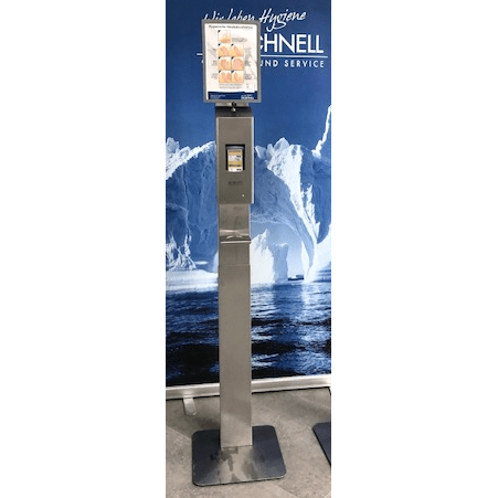 A stainless steel sanitizer dispenser stand with a DR.SCHNELL GmbH & Co. KGaA Dr. Schnell drip tray for dispensers and a digital instruction screen stands in front of icebergs and sea, creating a clear, modern atmosphere.