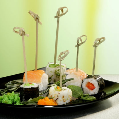A black plate with various sushi, each piece skewered with a PAPSTAR 40 finger food pick "pure" from PAPSTAR GmbH, garnished with herbs and roe, on a green-yellow surface - ideal for showcasing catering accessories.
