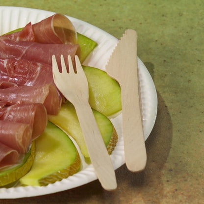 A white paper plate with green apple slices and rolled cured meat lies on a greenish textured surface, next to it a wooden fork and a PAPSTAR wooden knife "pure" 16.5 cm from PAPSTAR GmbH, environmentally friendly and stable.