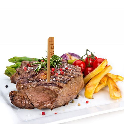 A grilled steak with the inscription "WELL" and a PAPSTAR 250 steak marker (9 cm, PAPSTAR GmbH) is served on a white plate with asparagus, cherry tomatoes, roasted onions, and French fries, garnished with rosemary and peppercorns.