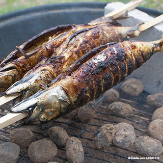 Two whole Steckerlfische are skewered on PAPSTAR grill skewers "pure" 80 cm (20 pieces) from PAPSTAR GmbH and grilled over glowing charcoal, with the skin charring and becoming crispy over the glowing coals.