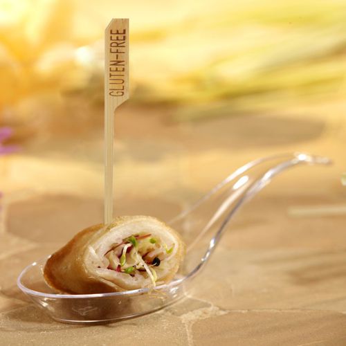 Eine mit Gemüse gefüllte Vorspeise sitzt auf einem durchsichtigen Kunststofflöffel, der mit einem PAPSTAR 250 Fingerfood - Spieße "pure" der PAPSTAR GmbH mit der Aufschrift "GLUTEN-FREE" gesichert ist. Der sanft verschwommene Hintergrund unterstreicht die Attraktivität des Fingerfoods für das Partybuffet.