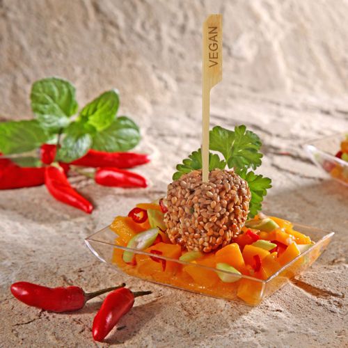 In einer kleinen durchsichtigen Schale befindet sich ein Mango-Gemüsesalat mit einer veganen Sesamkugel, serviert auf PAPSTAR 250 Fingerfood - Spieße "pure" von PAPSTAR GmbH. Mit Petersilie und Minze garniert, ist er ideal für Partybuffets, mit roten Chilischoten im Hintergrund.