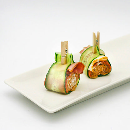 Two bites wrapped in cucumber slices are secured with PAPSTAR mini wooden clips (3.5 cm) from PAPSTAR GmbH, ideal for craft projects, and served on a cardboard tray (100 pieces) - perfect for creative party platters.