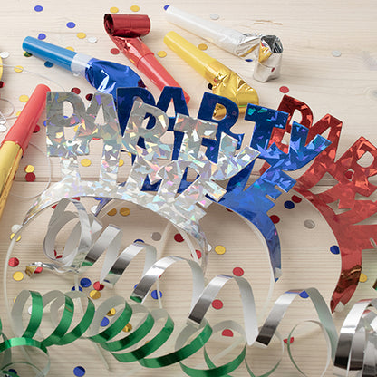 The PAPSTAR 4 headbands color assorted "Metallic" from PAPSTAR GmbH shine in bright metallic colors like blue, red, and silver - ideal for parties with confetti, wavy ribbons, and colorful noisemakers on a light wooden background.
