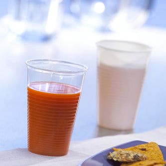 Ein Starpak 25 Trinkbecher, PP 0,2 l (Ø 7,03 cm · 9,9 cm), gefüllt mit Orangensaft, steht im Vordergrund neben einer weißen Tasse mit hellem Getränk; Unten rechts ist ein blauer Teller mit Essen zu sehen – ideal für unterwegs.