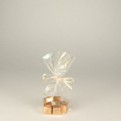 A PAPSTAR 300 bottom bag, cellophane "pure" transparent from PAPSTAR GmbH holds gold-wrapped candies tied with a light ribbon on a plain background – an elegant, sustainable touch with biodegradable packaging.