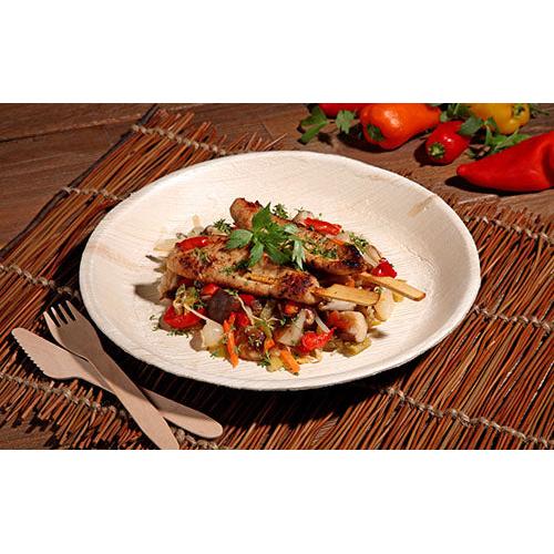 Grilled chicken skewers with a colorful vegetable pan are served on a PAPSTAR 6 plate, palm leaf "pure" round by PAPSTAR GmbH - environmentally friendly tableware, stylishly presented on a woven mat with wooden cutlery and fresh bell peppers in view.
