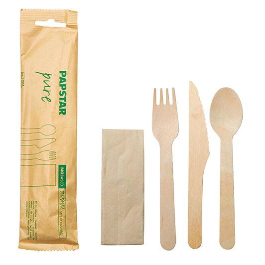 Ein PAPSTAR Besteckset, Holz „pure“ (Messer, Gabel, Löffel, Serviette in Papierbeutel) von PAPSTAR GmbH liegt neben einer braunen Serviette und einem Papierbeutel mit der Aufschrift „PAPSTAR pure“.
