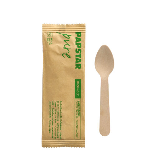 Ein PAPSTAR 11 cm Holz-Kaffeelöffel aus der „pure“-Serie liegt neben seinem einzeln verpackten Papierbeutel mit grünem PAPSTAR-Aufdruck; 50 Stück pro Packung, nachhaltig hergestellt von PAPSTAR GmbH.